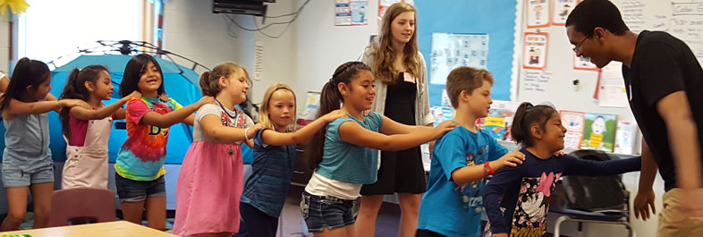Image of elementary students forming a human train in a classroom with two teachers